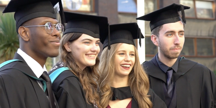 four students in graduation robes smiling