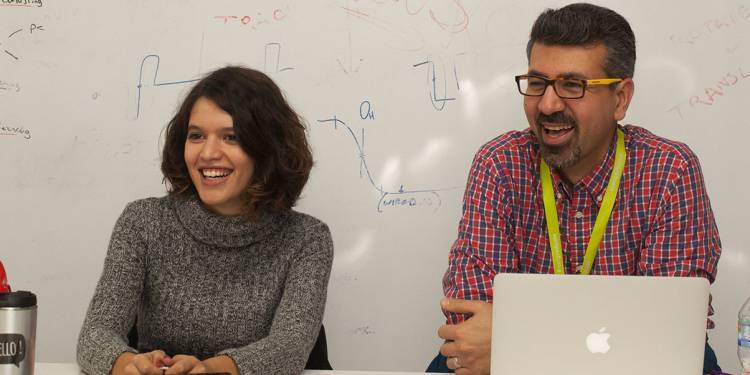 Student services man and student sat at desk smiling.