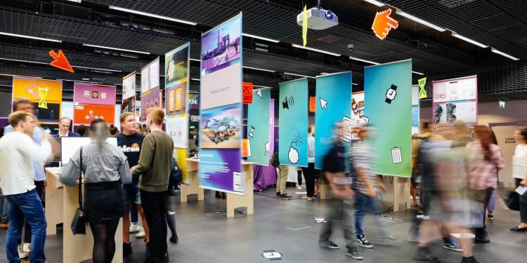An exhibition with lots of bright coloured posters hanging from the ceiling, with people blurred in the foreground