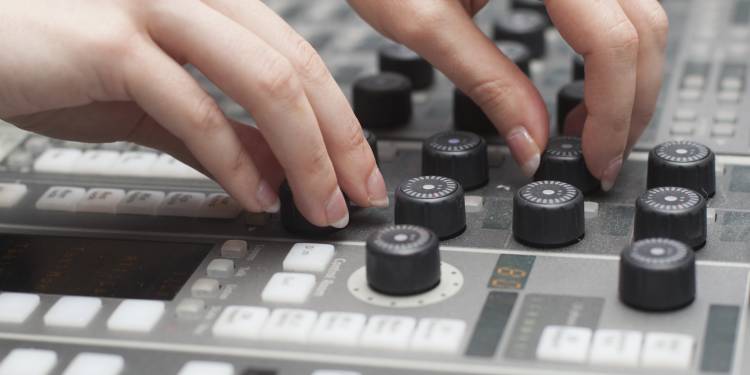 A pair of white hands using a mixing desk, to turn dials and push buttons