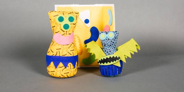 3 small brightly coloured sculptures, similar to body shaped with bright coloured eyes sit on a grey background.