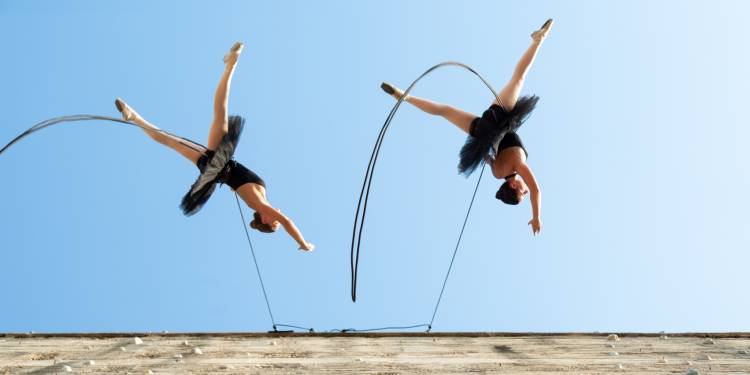 Two ballerinas perform while suspended from a building