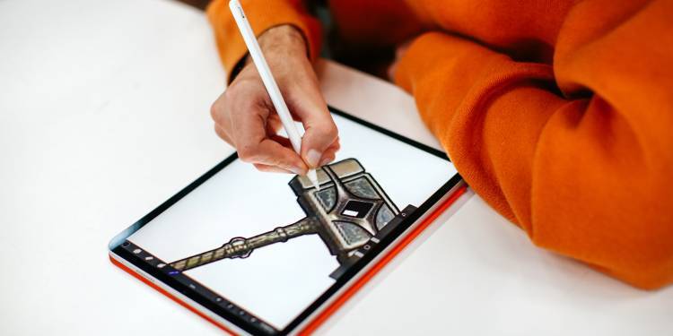 persono in a bright orange jumper draws a hammer on an ipad