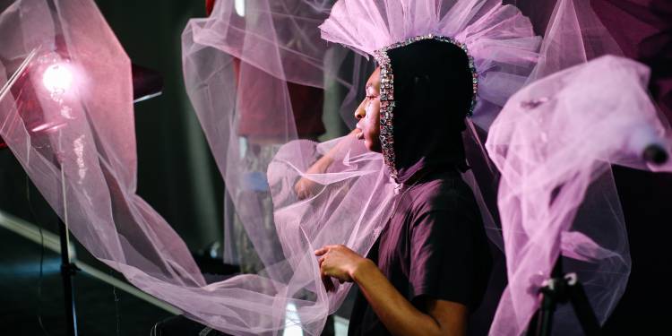 Photography studio set up with a young black male in the foreground draped in pastel pink chiffon