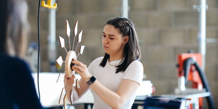 young white woman with dark brown shoulder length hair glueing hands to a wooden clock