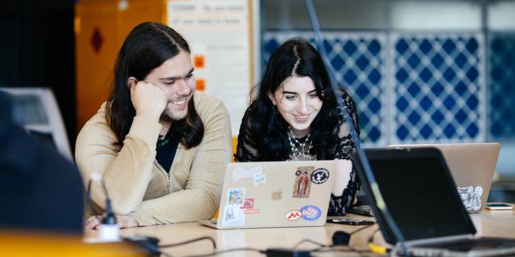 A man and a woman smiling while looking at a laptop screen 