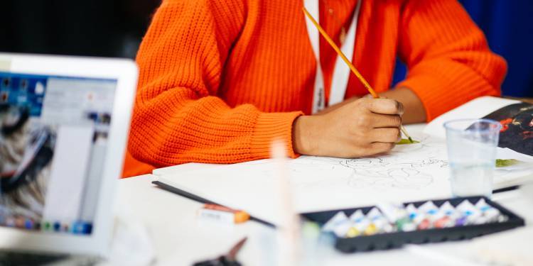 woman in orange jumper painting on a notepad