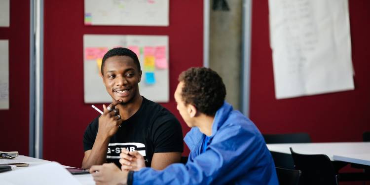 Two males sit at a table in a classroom deep in discussion