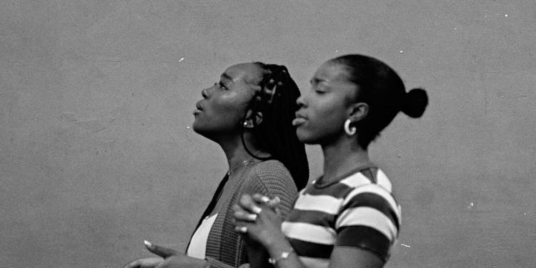 Two women stand with their hands in prayer