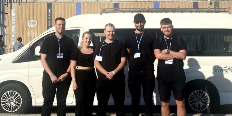 Five Ravensbourne students stand in a line in front of a COP27 sign in Egypt