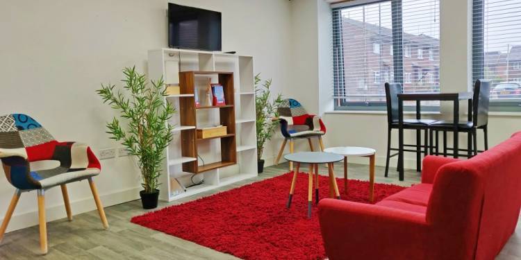 Inside the communal space of The Cube, a sofa, table and chairs shelves and a TV on the wall. 