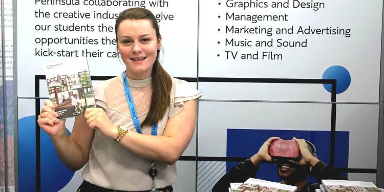 Young woman sits at desk holding up a university prospectus