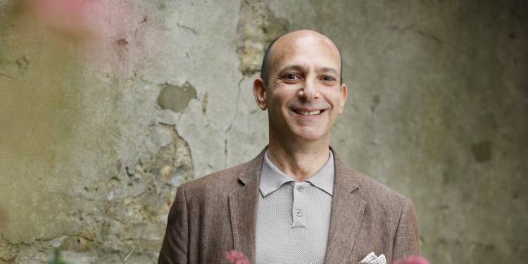 Shaun Borstrock smiles in front of an old wall with flowers in the foreground