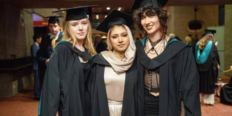 Three women pose in gowns inside Barbican building