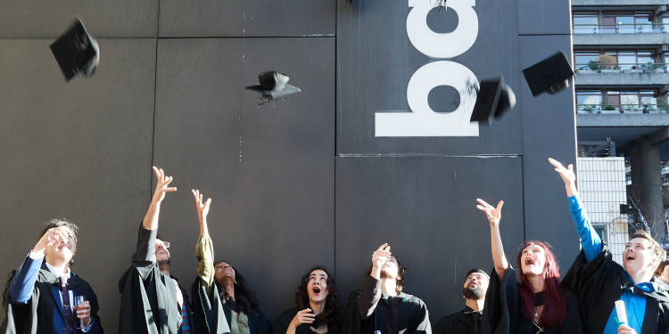 Stdents otside the barbican in graduation robes throwing hats in the air