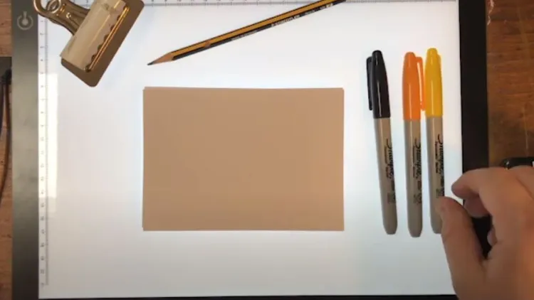 a bulldog clip, square pieces of paper, pencil and three marker, one yellow, one orange, one black.