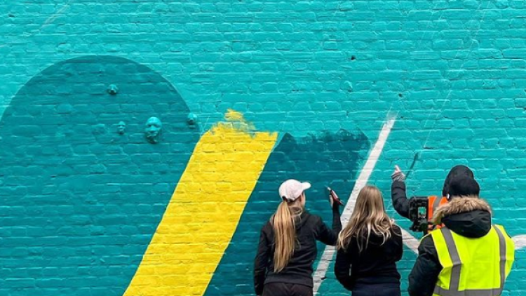 Two females sit in front of mural wall