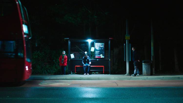 People stood at a dimly-lit bus stop with bus approaching to the left