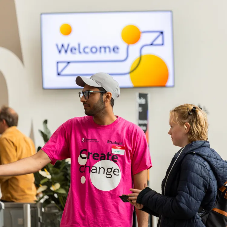 Student ambassador in a pink t-shirt welcoming visitors to open day in R1 at Ravensbourne University