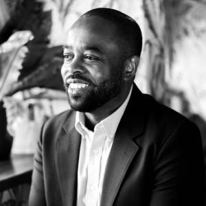 Black and white image of Lawrence Lartey smiling and wearing a white shirt and suit jacket