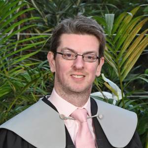 man with glasses wearing a pink tie and shirt with palm leaves behind him