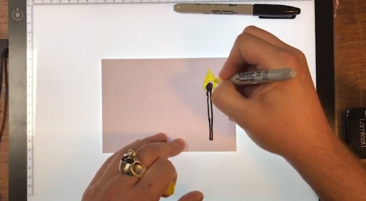 a pair of hands using a yellow marker pen to colour in a flame