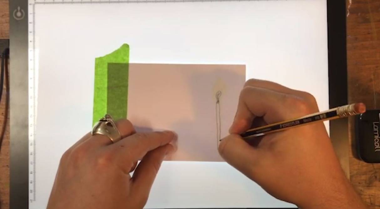 a pair of hands using a pencil to sketch a match onto a stack of A6 paper