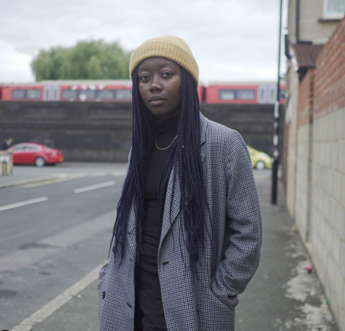 Girl stands at side of road wearing a long coat and beanie hat