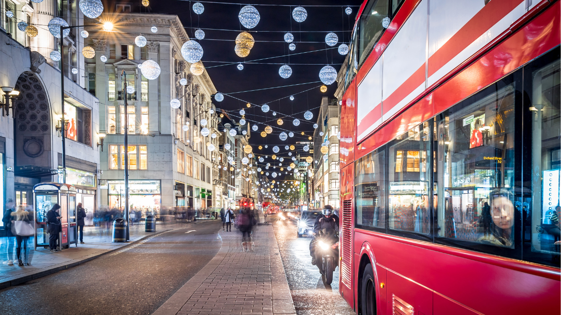 A red bus travels down Oxford Street which is decorated with Christmas lights