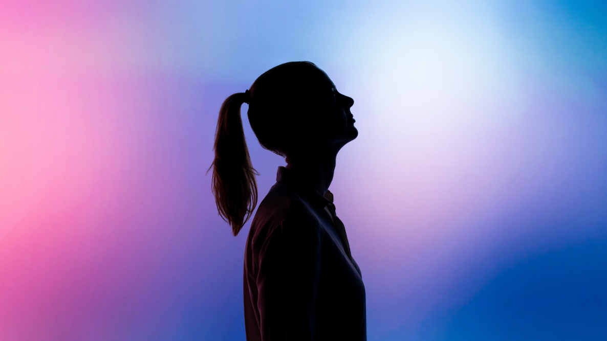 A silhouette of a girl looks upward surrounded by a pink and blue haze