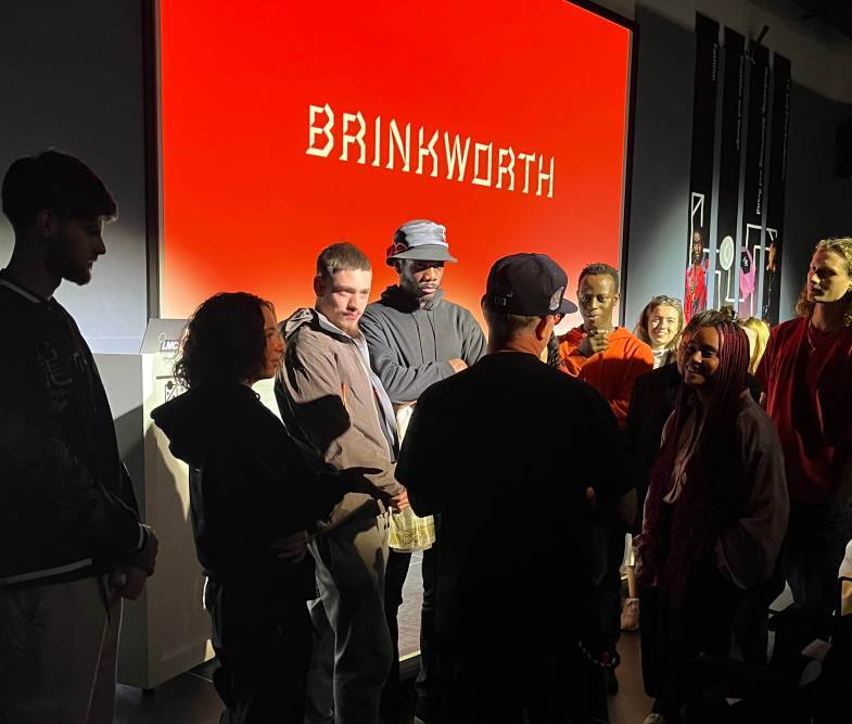 A crowd of students at the rave Late event standing, the Brinkworth logo is on the big screen in the background. 