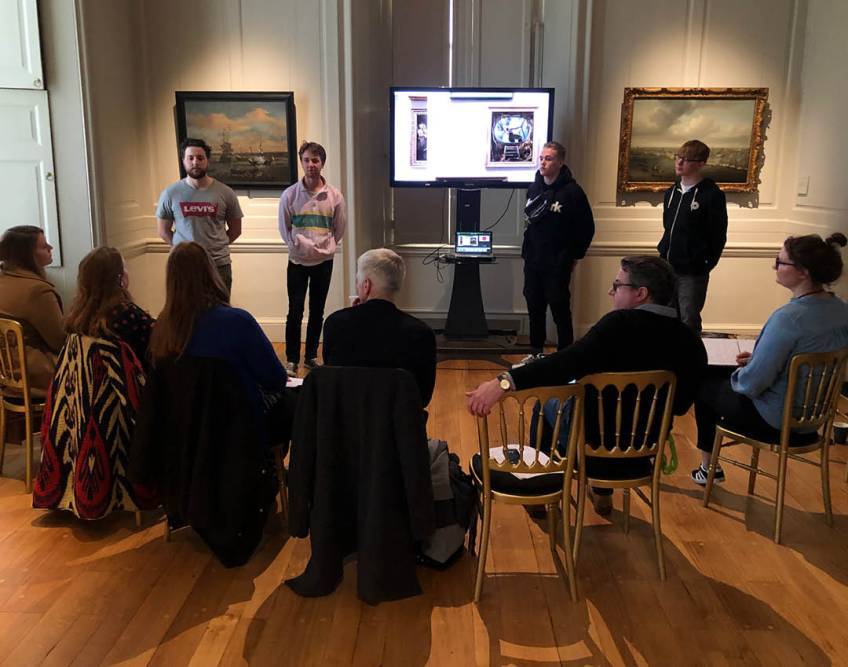 Students pitching to a panel in an art gallery