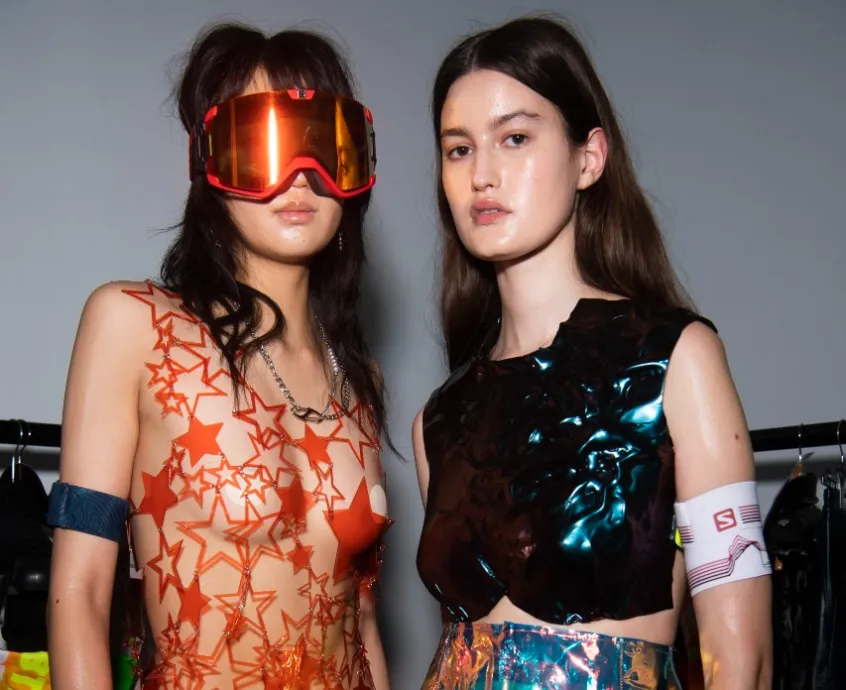 Two models pose next to each other one wearing red sky goggles