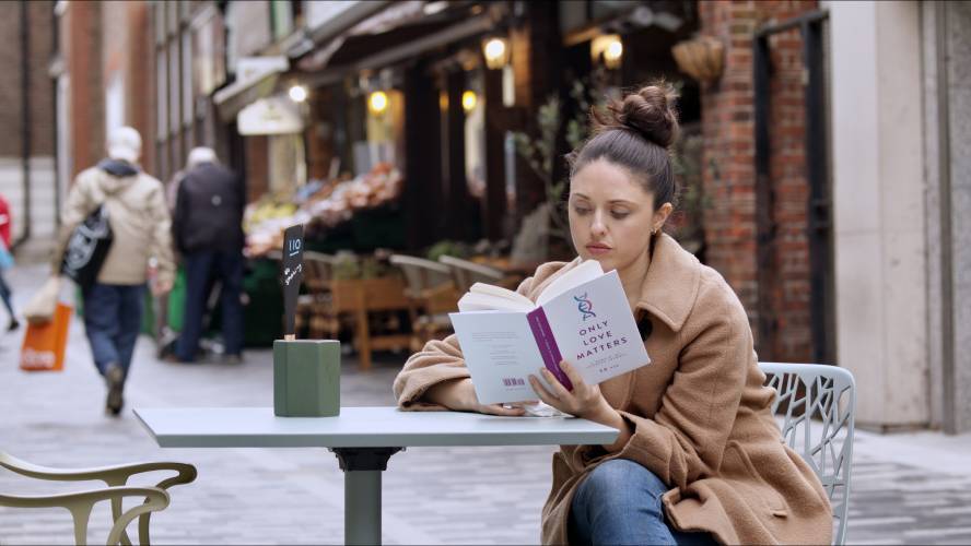 A young woman reads a book outside a London street cafe