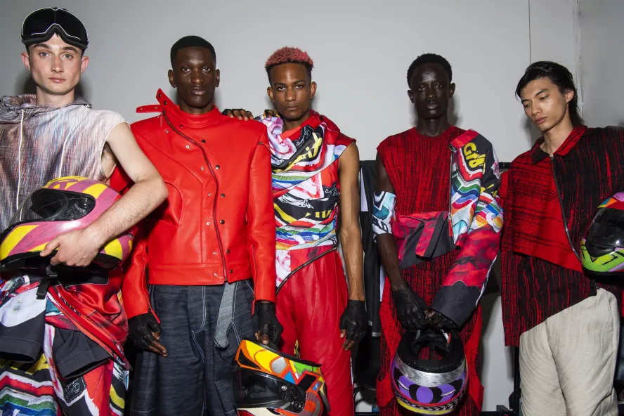 Male models wearing edgy leather outfits holding motorbike helmets