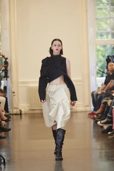 Model wears chic black top with white skirt and boots