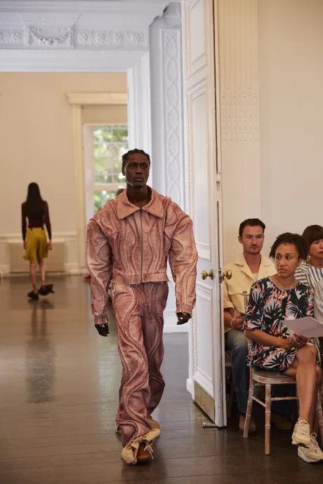 Male model wears matching pink jacket and trousers with swirling pattern