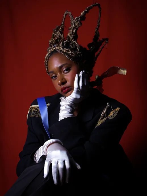 Young woman dressed royally poses with her hand on her cheek