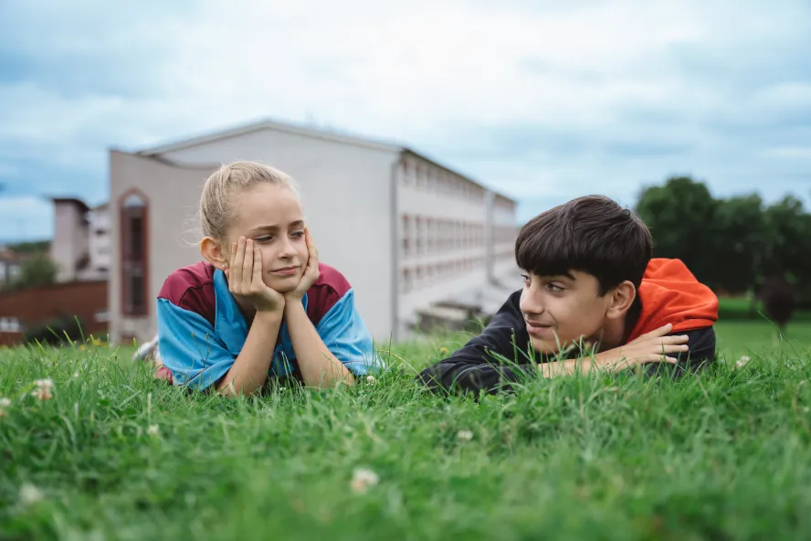 A girl in a football shirt and a boy lay in the grass