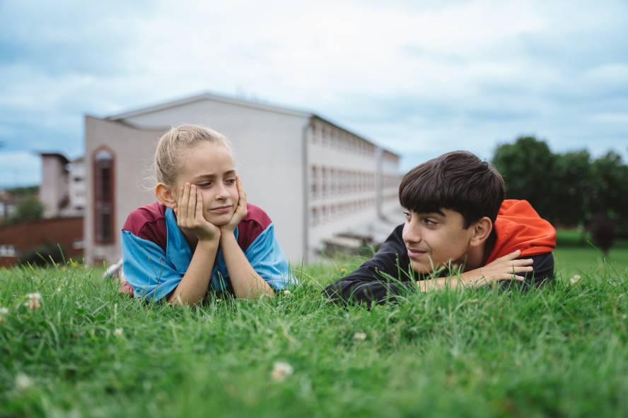 A girl in a football shirt and a boy lay in the grass
