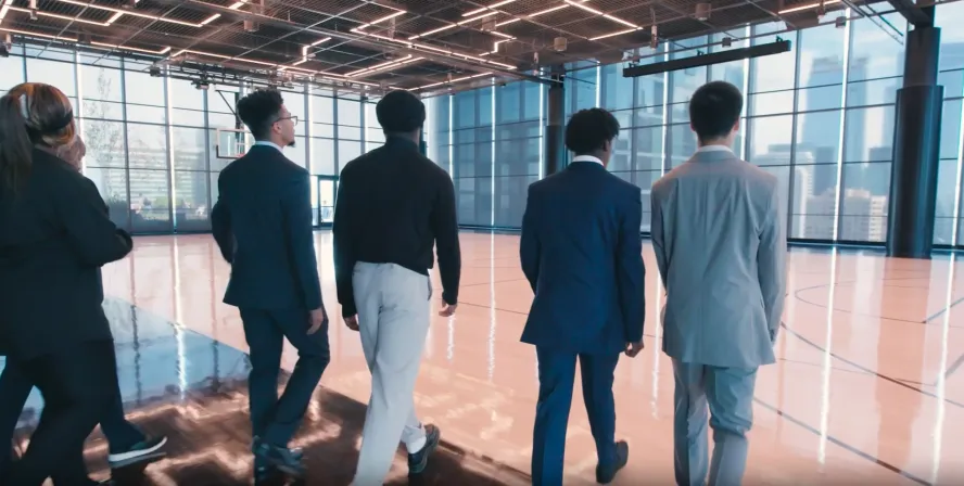 Five men in suits walk across an indoor basketball court
