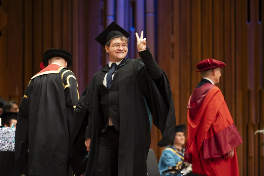 Graduate gives peace sign on stage at graduation