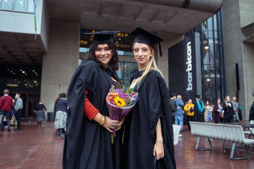 Two female graduates pose with flowers outside Barbican building
