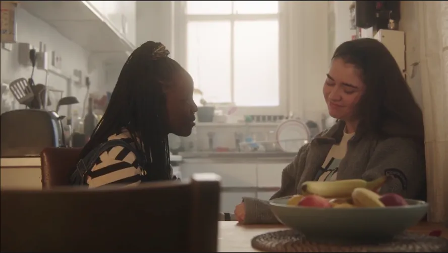 two women sat in at the kitchen table in conversation, one consoling the other.