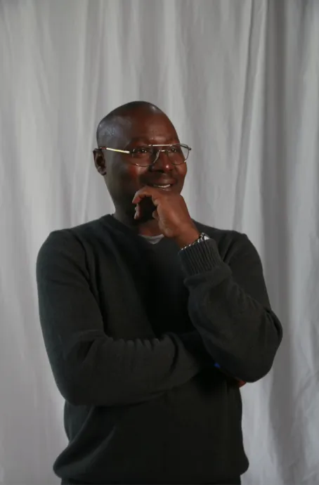 Smiling black man with bald head in glasses smiling with his hand against his face