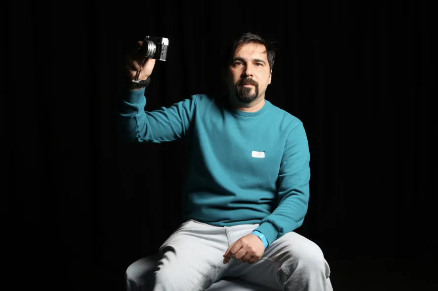 Man in blue jumper holding a camera against a black background