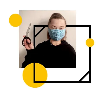 a photo of a white woman with her hair up, wearing a handmade light blue face mask, holding a pair of fabric scissors in left hand