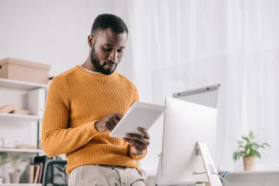  Concentrated african american designer in yellow sweater working with digital tablet in modern office