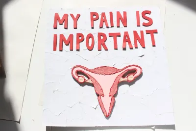 white square placard with red text reading my pain is important with an embrodered womb underneath