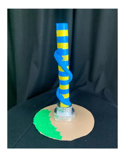 Small scultpture with blue and yellow striped cylinder stands tall with green cardboard base and a blue slide round the tall sculpture